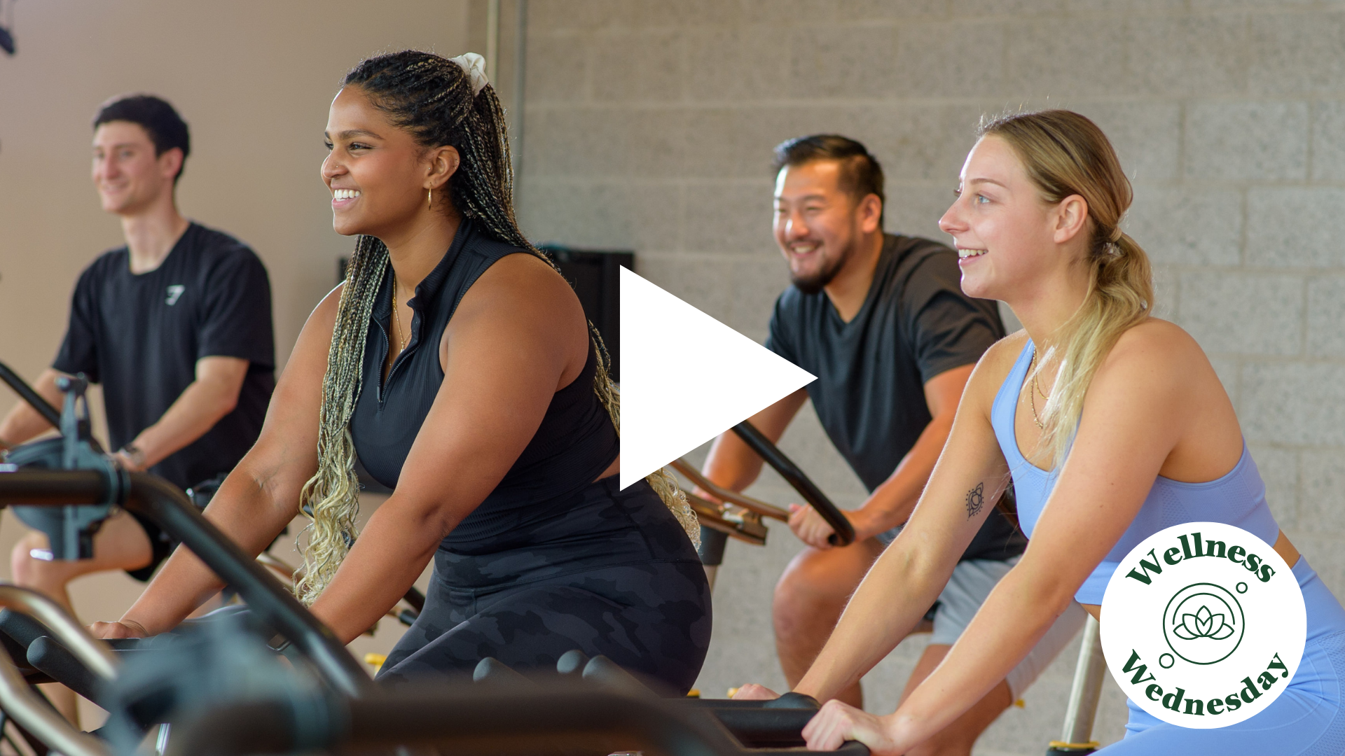 4 individuals on cardio bikes working out, smiling. 